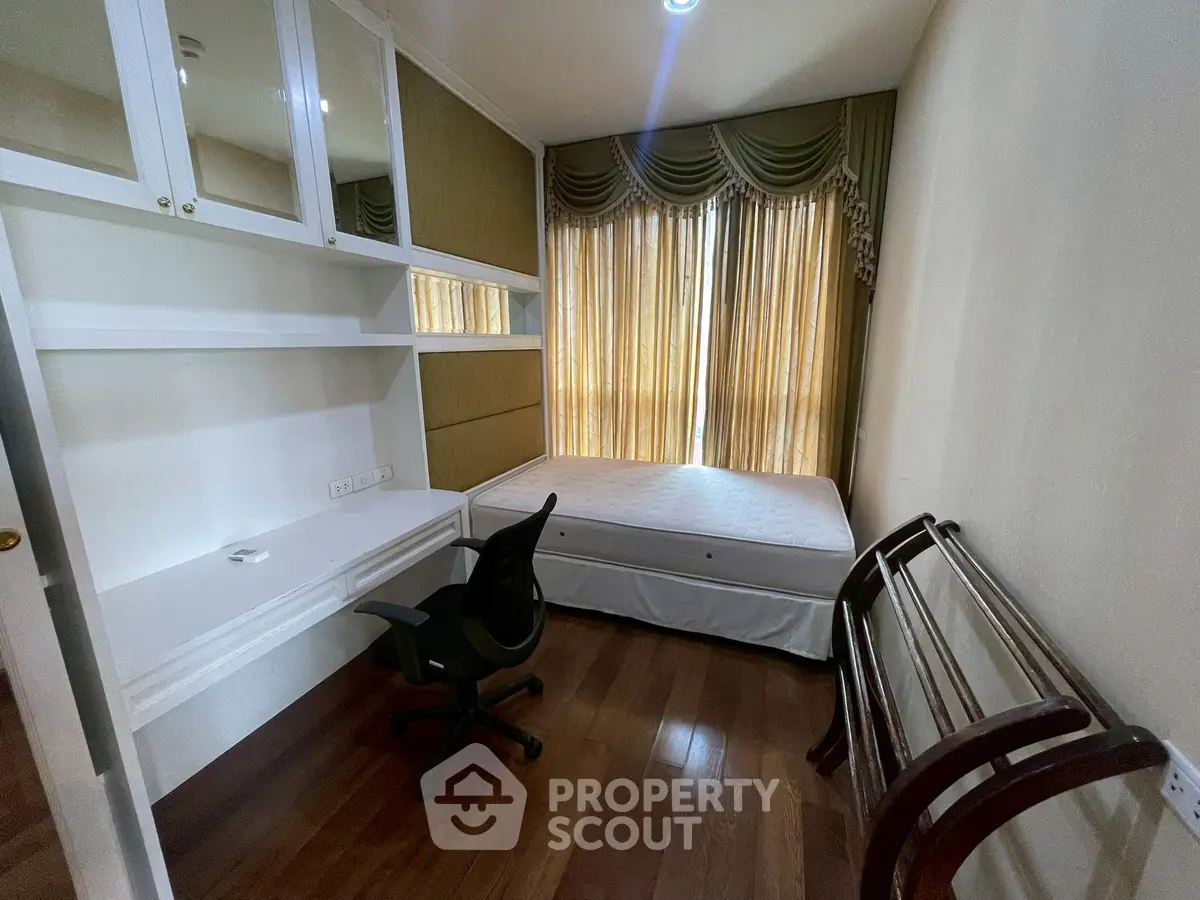 Cozy bedroom with wooden flooring, built-in desk, and elegant curtains in a modern apartment.