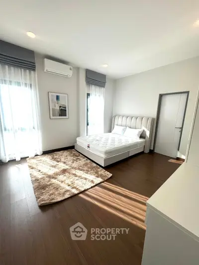 Spacious bedroom with modern decor, large windows, and hardwood floors in a bright, airy apartment.