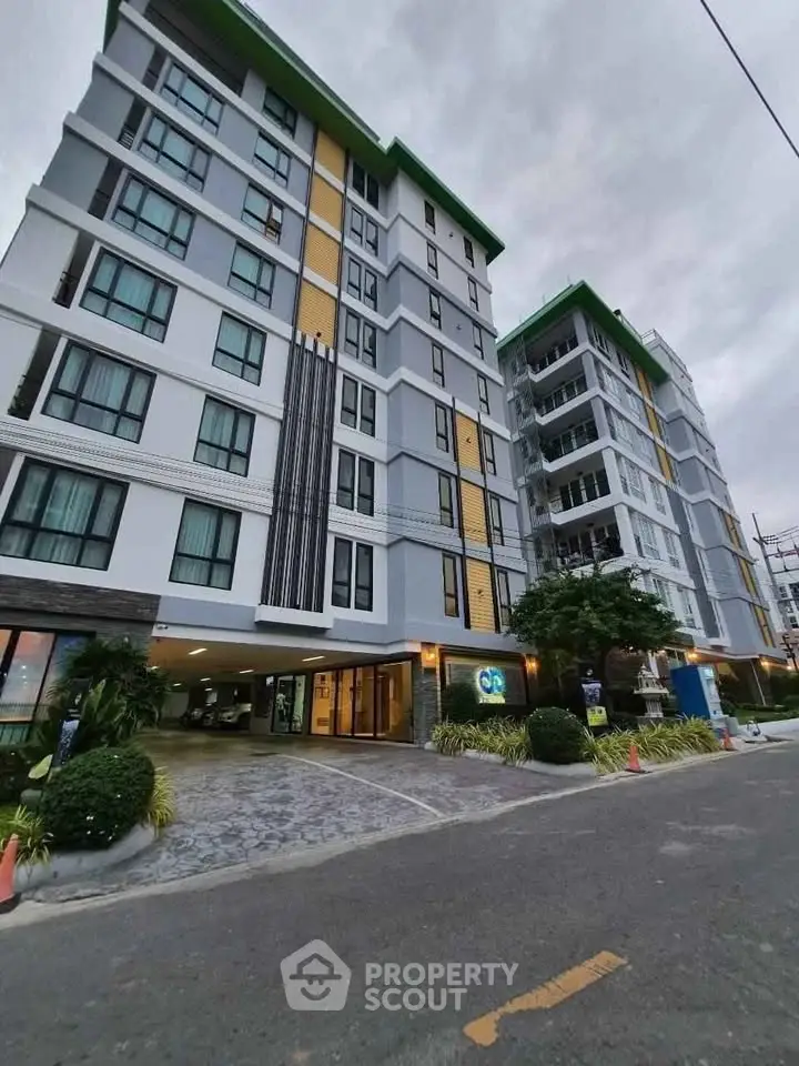 Modern multi-story residential building with landscaped entrance and parking area.