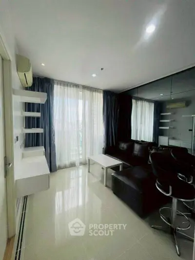 Modern living room with sleek black sofa and large windows offering natural light.