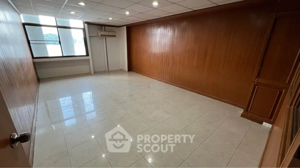 Spacious unfurnished room with wooden paneling and large window ideal for office or study.