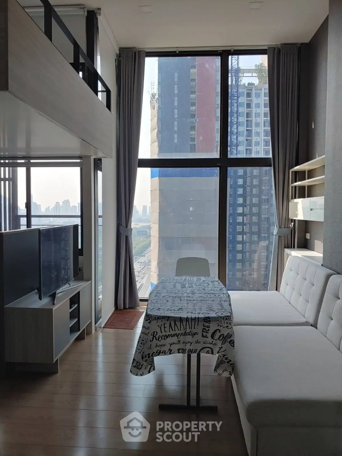 Modern living room with floor-to-ceiling windows and city view, featuring a cozy sofa and TV setup.