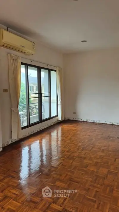 Spacious living room with wooden flooring and large windows offering natural light.