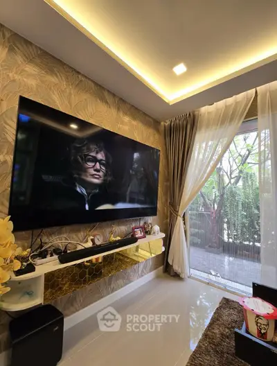 Stylish living room with large TV, elegant decor, and garden view through sheer curtains.