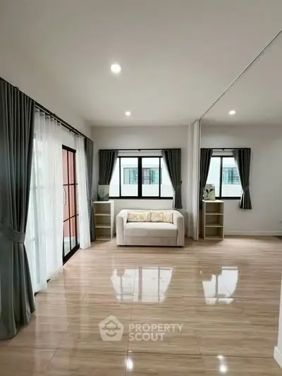 Spacious living room with large windows and elegant curtains, featuring a cozy sofa and polished wooden floors.