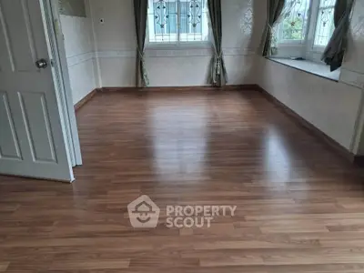 Spacious empty room with elegant wooden flooring and large windows for natural light.