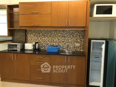 Modern kitchen with wooden cabinets, mosaic backsplash, and appliances including fridge and microwave.