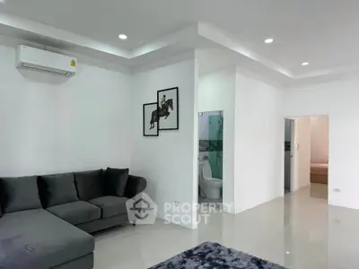 Modern living room with sleek design, featuring a cozy gray sofa and contemporary artwork, leading to a stylish bathroom.