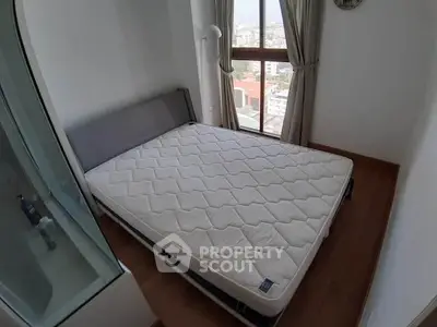 Cozy bedroom with large window offering city views, featuring a comfortable bed and wooden flooring.