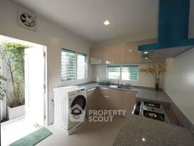 Modern kitchen with sleek countertops, gas stove, and washing machine, featuring ample natural light and garden view.
