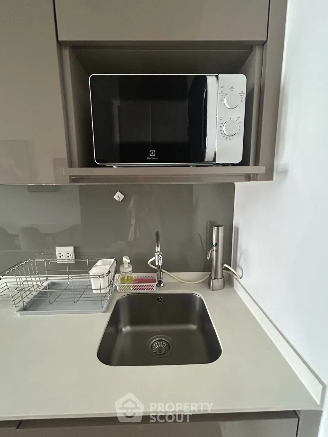 Modern compact kitchen with sleek cabinetry and built-in microwave, featuring a stainless steel sink and minimalist design.