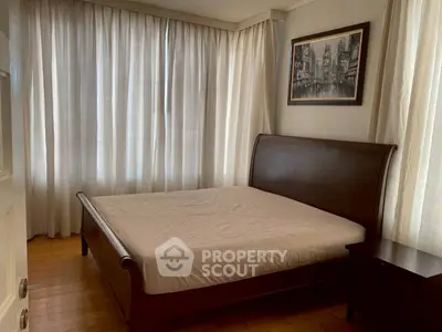 Cozy bedroom with elegant wooden bed and soft natural light from large windows.