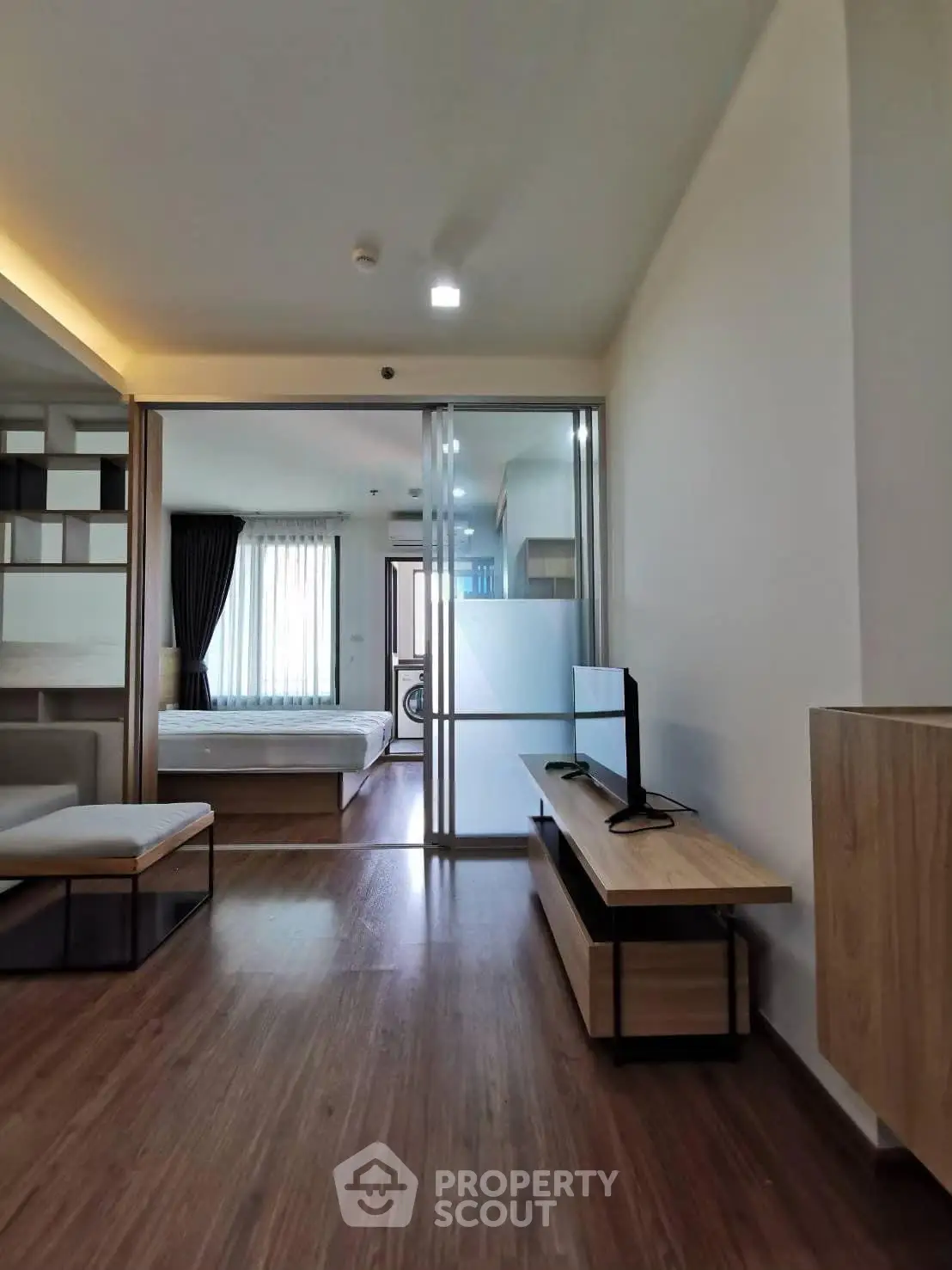 Modern apartment interior with open layout, featuring a cozy living area and bedroom separated by glass doors.