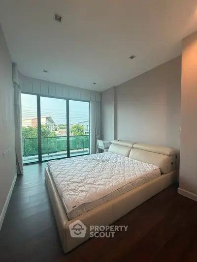 Spacious bedroom with large windows and balcony access, featuring a modern bed and serene outdoor view.