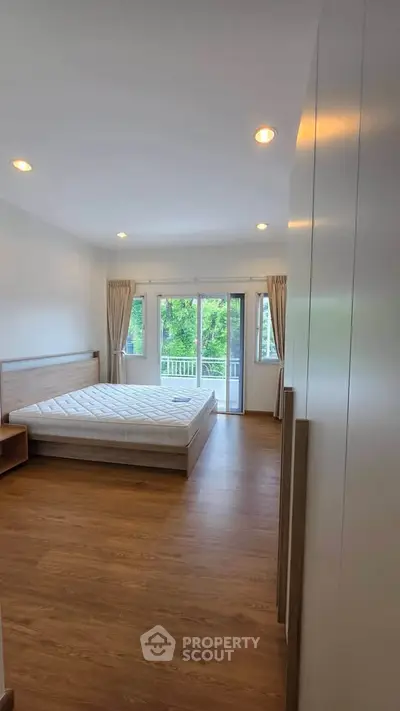 Spacious bedroom with large windows and balcony access, featuring elegant wooden flooring and modern lighting.