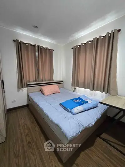 Cozy bedroom with wooden flooring and modern furnishings, featuring a comfortable bed and stylish curtains.
