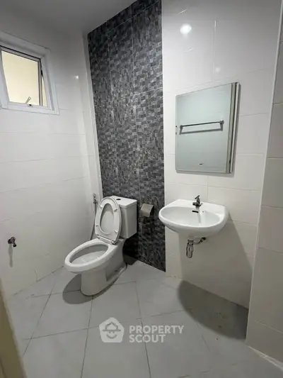 Modern bathroom with sleek design and tiled walls, featuring a toilet and sink.
