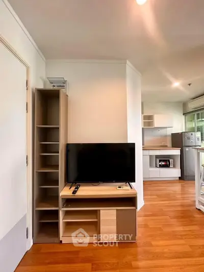 Modern living room with TV and open kitchen layout, featuring sleek wooden flooring and contemporary design.