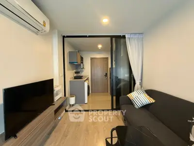 Modern living room with sleek furniture and glass partition leading to a compact kitchen.