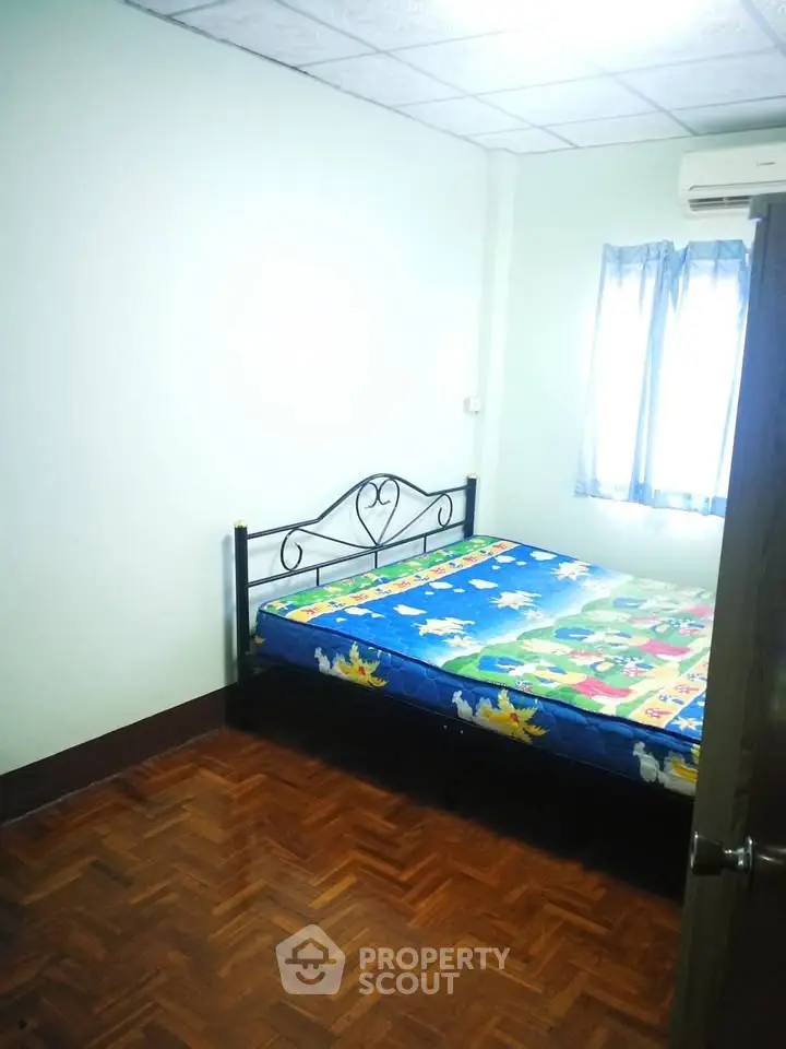 Cozy bedroom with wooden flooring and natural light, featuring a comfortable bed and air conditioning.