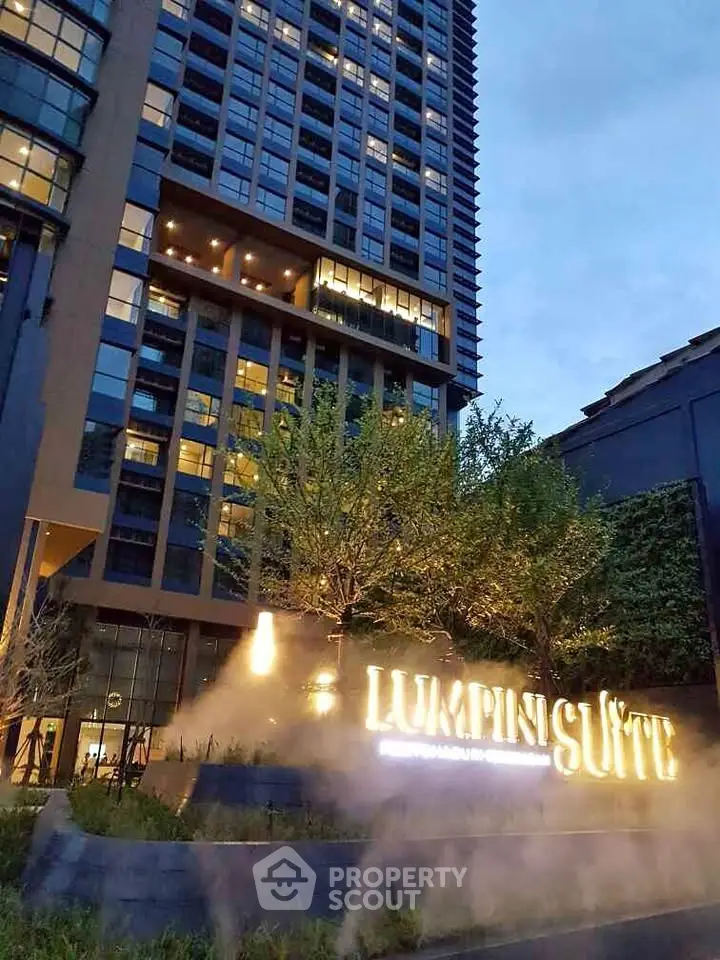 Luxurious high-rise building exterior with illuminated signage and lush greenery at dusk.