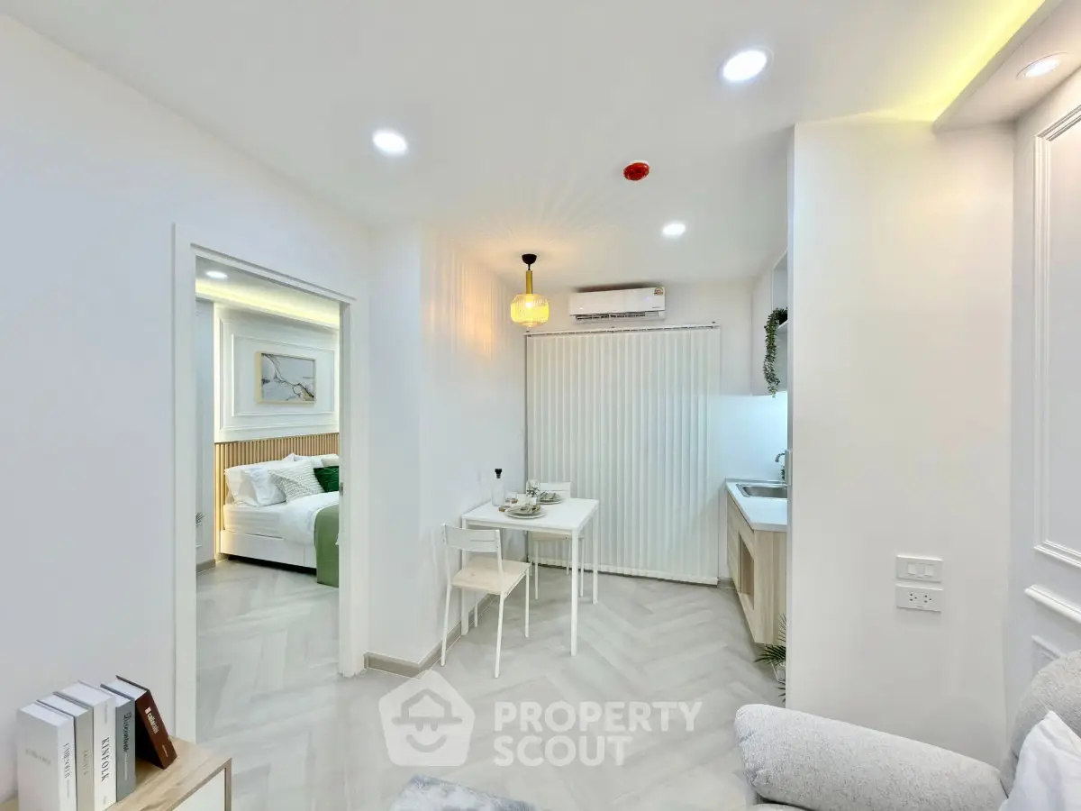 Modern open-plan living room with dining area and view into a cozy bedroom, featuring stylish decor and bright lighting.