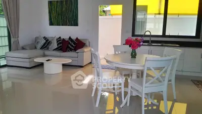 Spacious living room with modern decor and open kitchen layout, featuring a cozy sofa and elegant dining area.