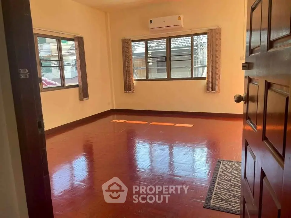 Spacious empty room with wooden flooring and large windows, perfect for customization.