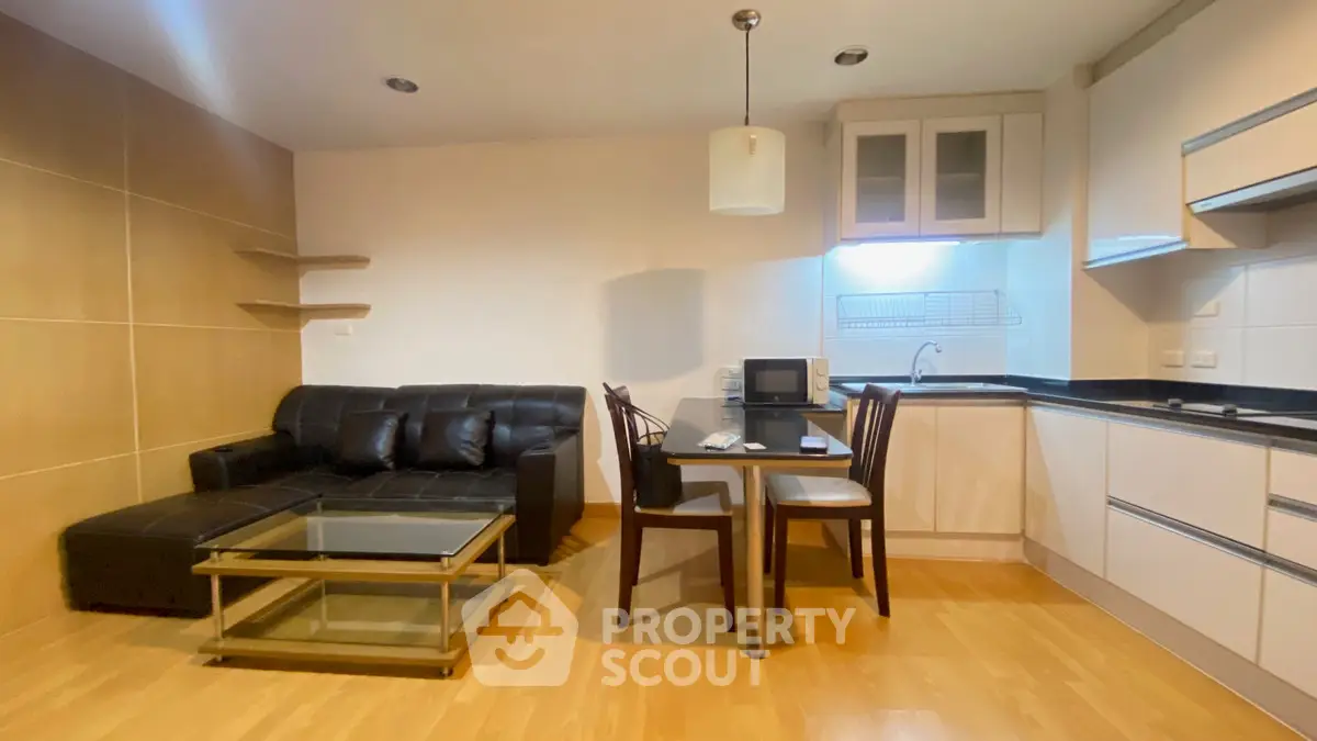 Modern open-layout living room with kitchen, featuring sleek furniture and wooden flooring.