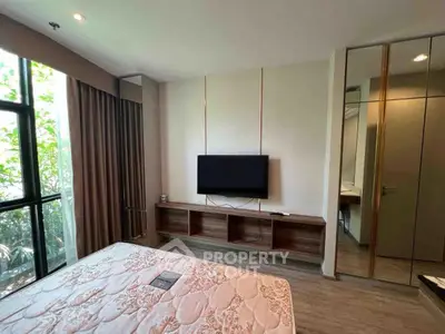 Modern bedroom with large window and wall-mounted TV, featuring elegant decor and ample natural light.