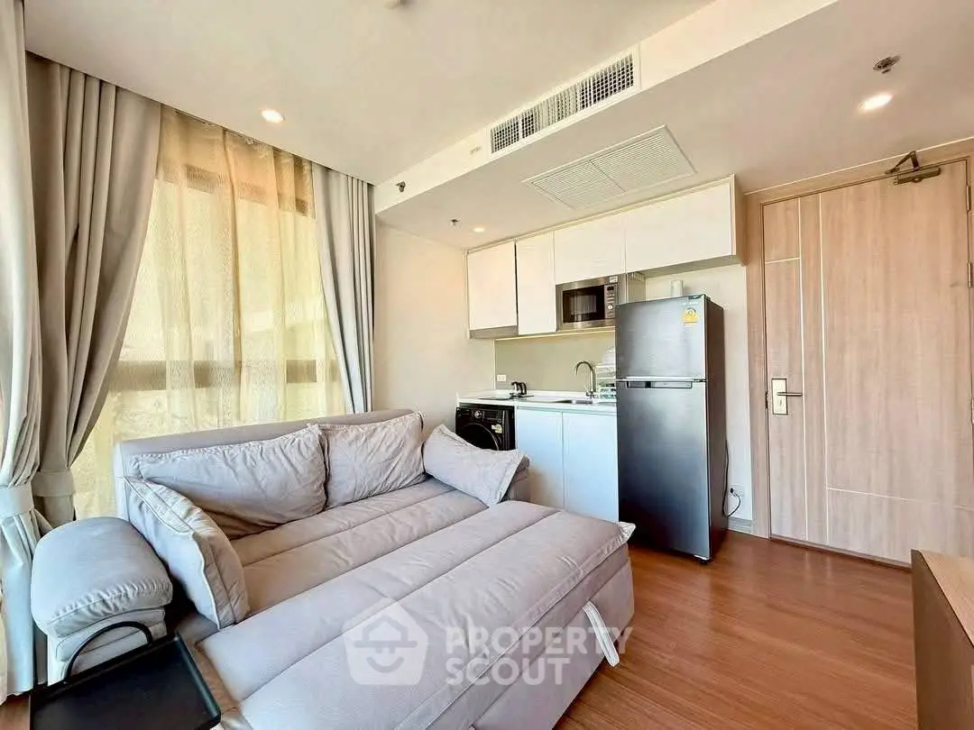 Modern living room with cozy sofa and compact kitchen in open layout apartment.