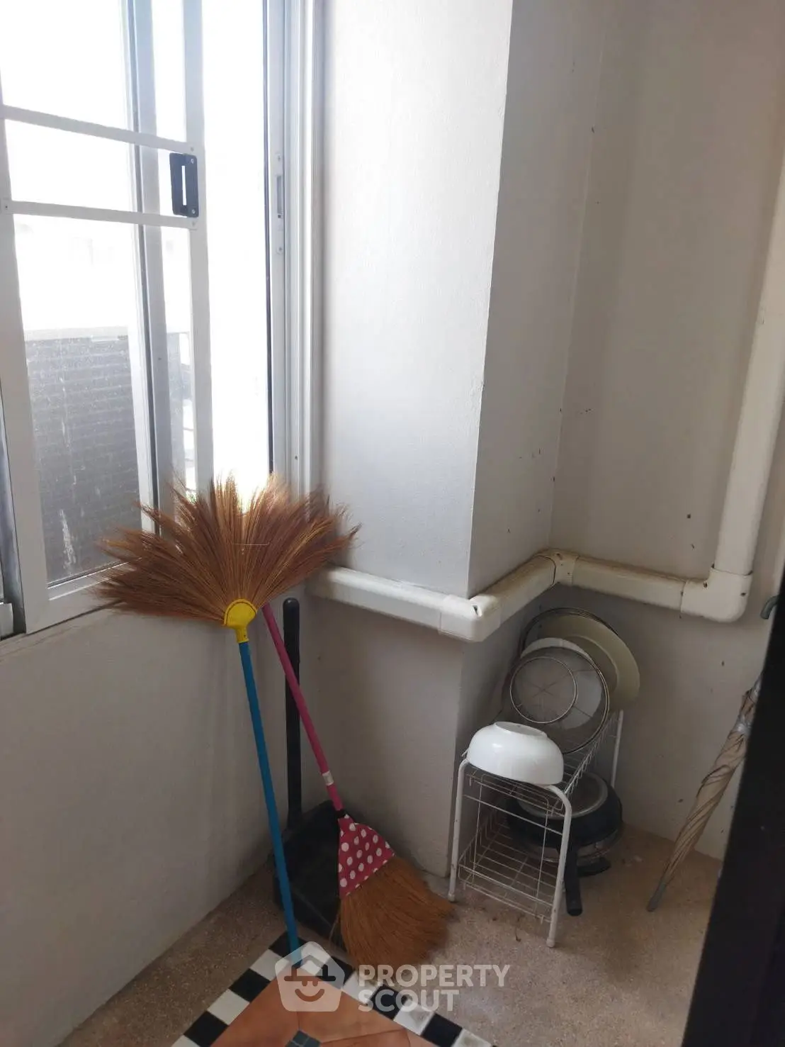 Cozy utility corner with brooms and dish rack by a window, perfect for small apartments.