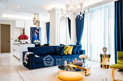 Luxurious living room with elegant blue sofa and chandelier, featuring modern decor and ample natural light.