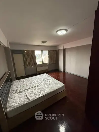 Spacious bedroom with wooden flooring and large windows in a modern apartment.