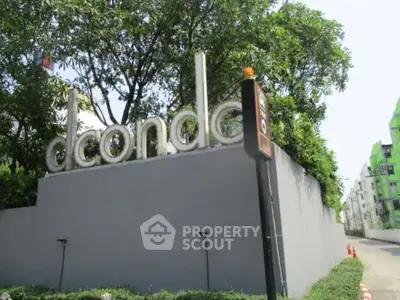 Modern condo entrance with lush greenery and sleek signage in urban setting.