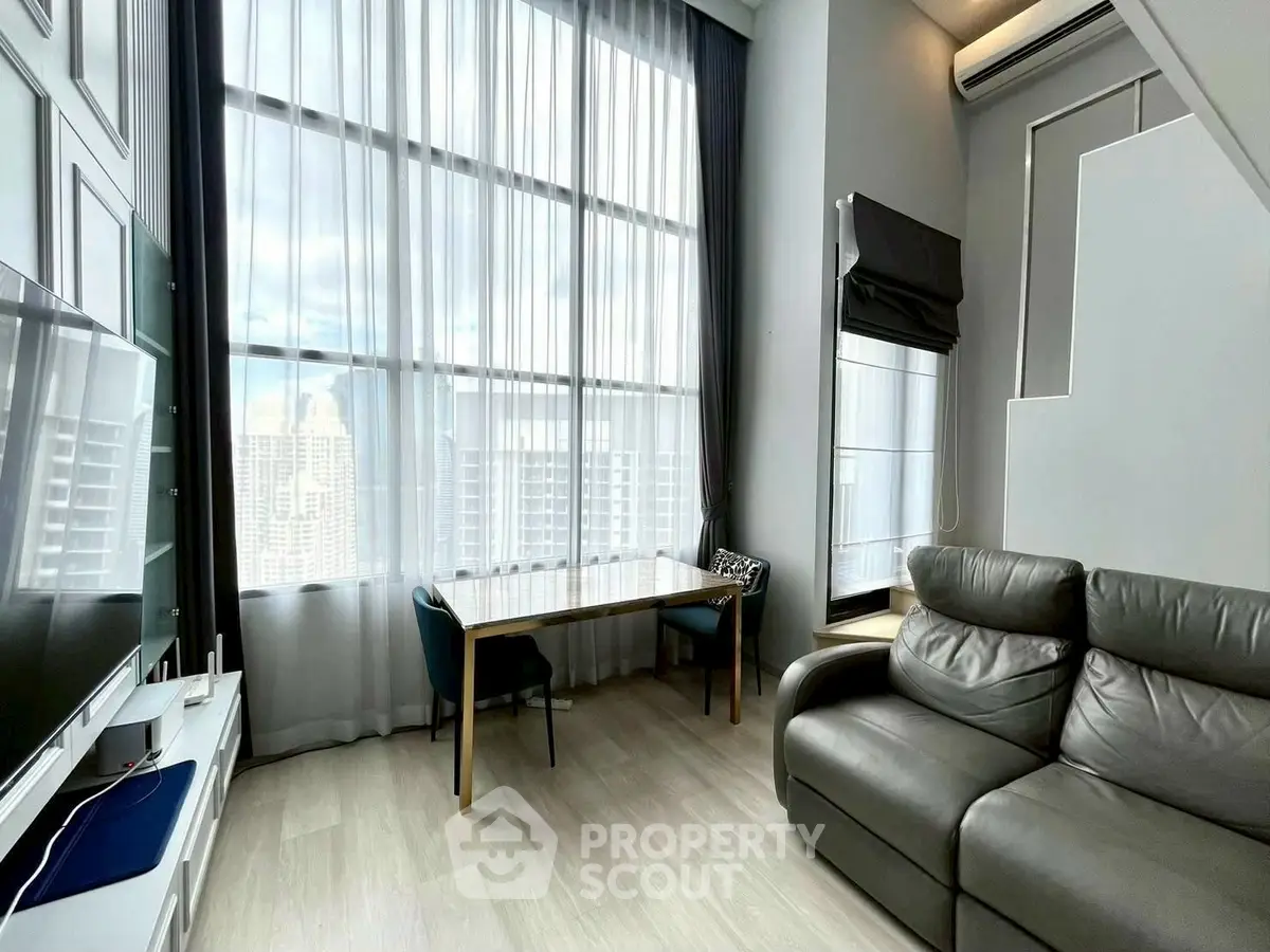 Modern living room with high ceilings and large windows offering city views.