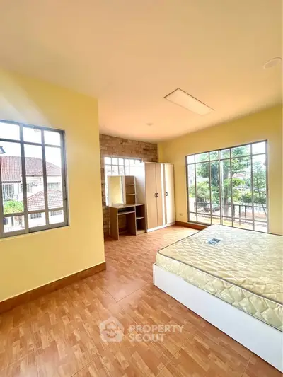 Spacious bedroom with large windows and wooden flooring, offering a bright and airy atmosphere.