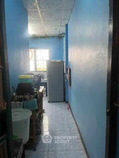 Compact storage room with blue walls and tiled floor, featuring a refrigerator and various household items.