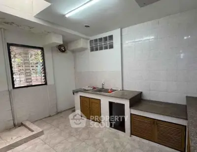 Spacious kitchen with tiled walls and countertops, featuring a window for natural light.