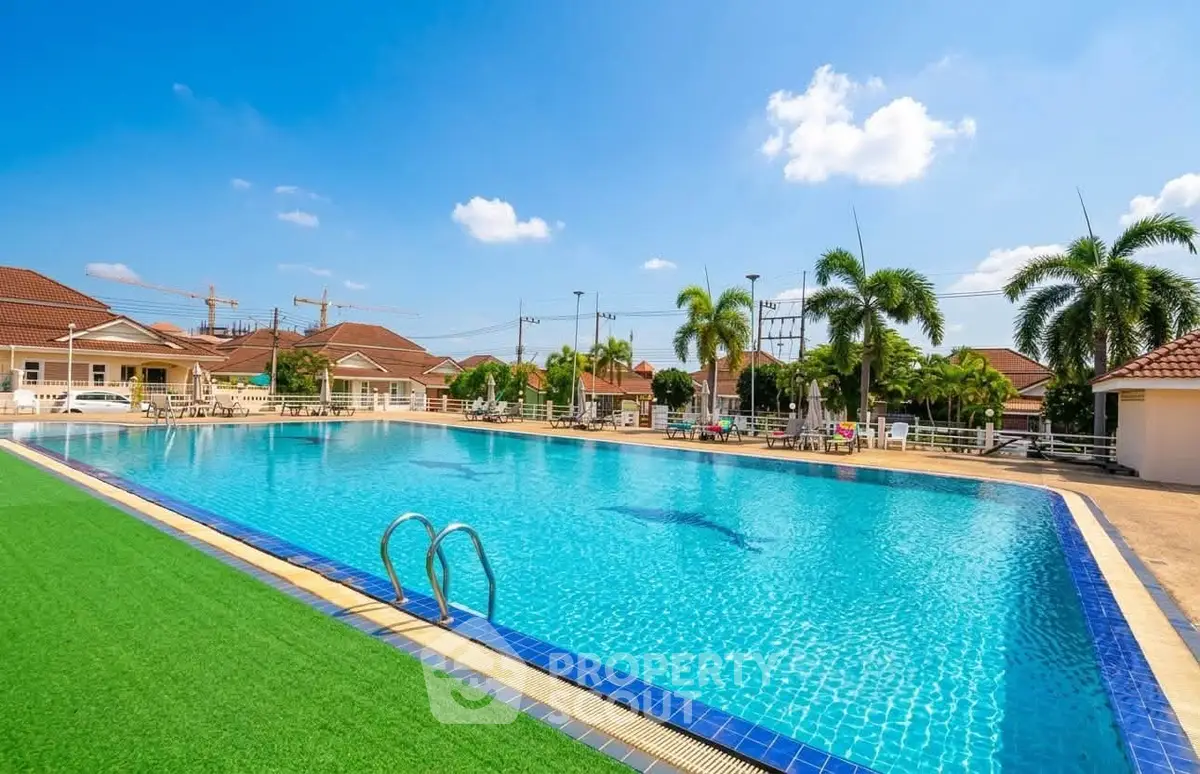 Luxurious residential pool with clear blue water and palm trees under a sunny sky.