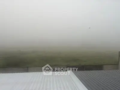 Foggy view over rooftops with distant greenery and fence, serene and tranquil atmosphere.