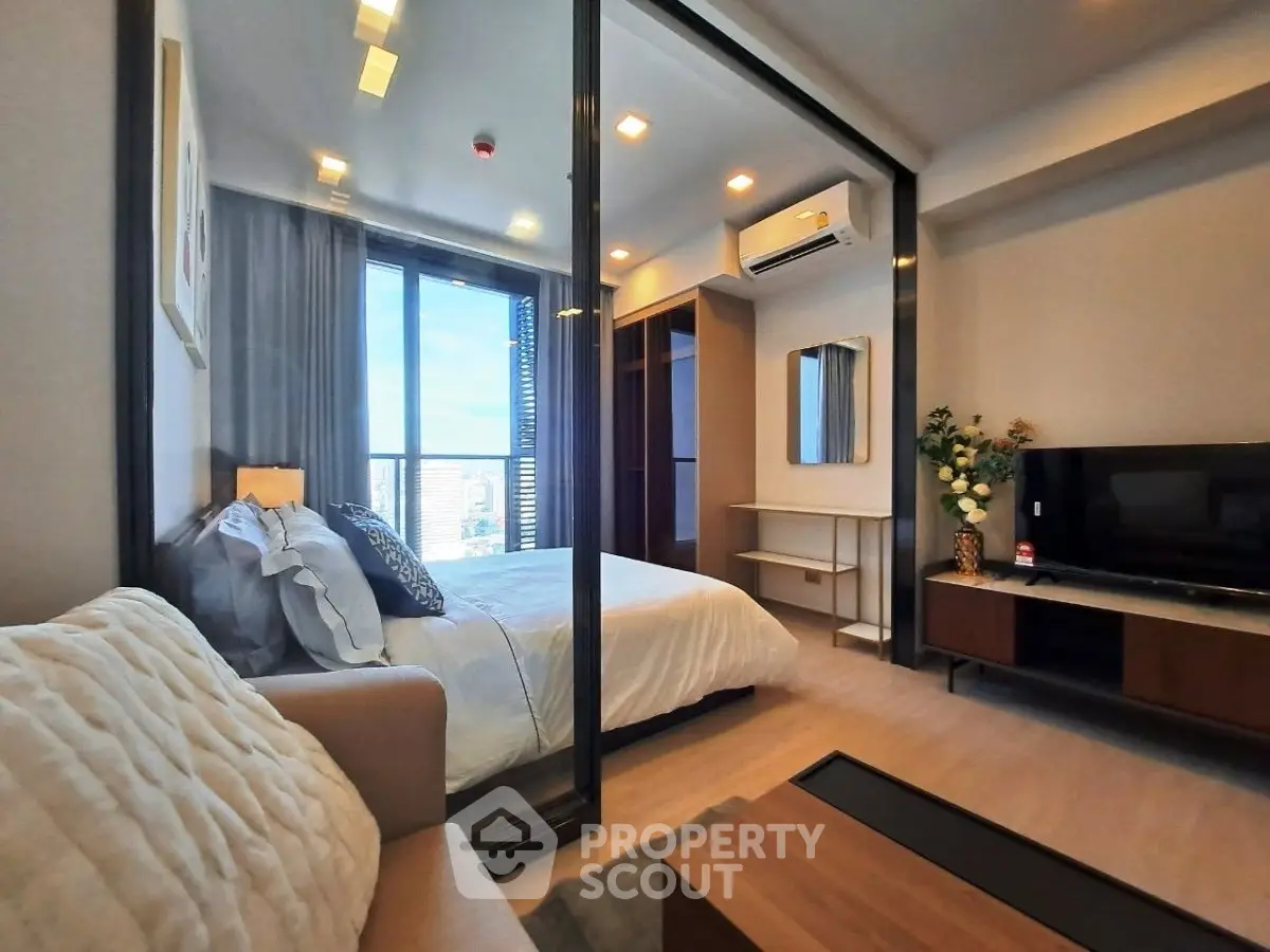 Modern bedroom with glass partition, cozy seating, and city view balcony in luxury apartment.