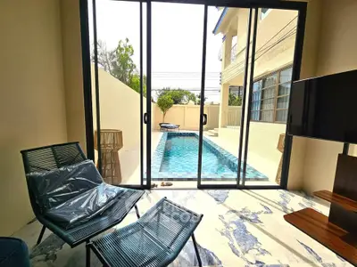 Luxurious living room with pool view through glass doors, featuring modern furniture and elegant flooring.
