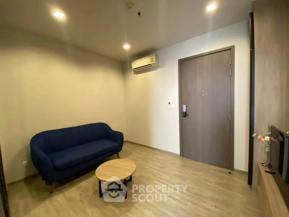 Modern living room with blue sofa, wooden flooring, and air conditioning unit.