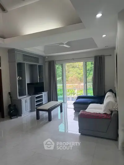 Spacious living room with modern decor and large windows offering lush green views.