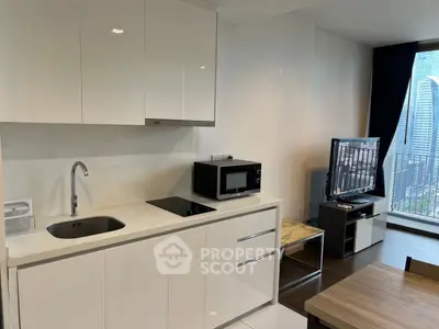 Modern kitchen with sleek white cabinets and open layout, featuring a microwave and TV near a balcony view.