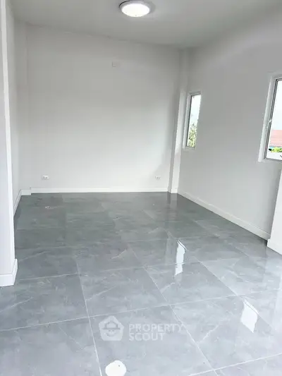 Spacious empty room with glossy tiled flooring and natural light.