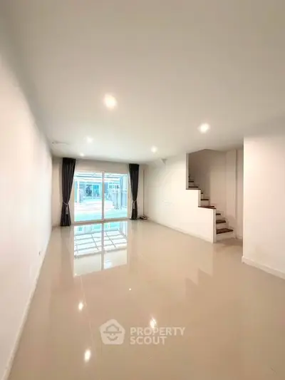 Spacious modern living room with large windows and staircase, perfect for family gatherings.