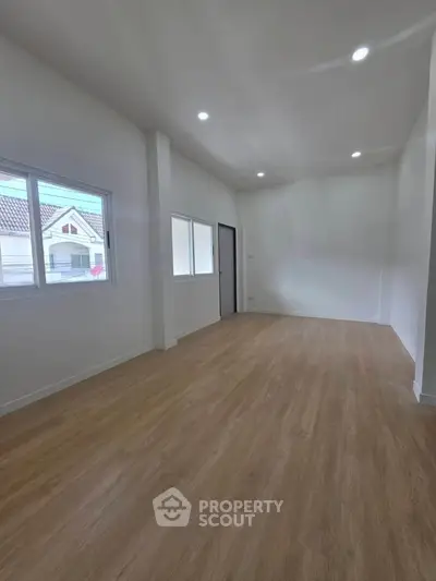 Spacious empty room with wooden flooring and large windows, ideal for customization.