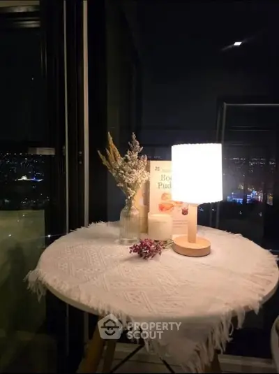 Cozy night view from a balcony with a lit table lamp and decorative flowers.